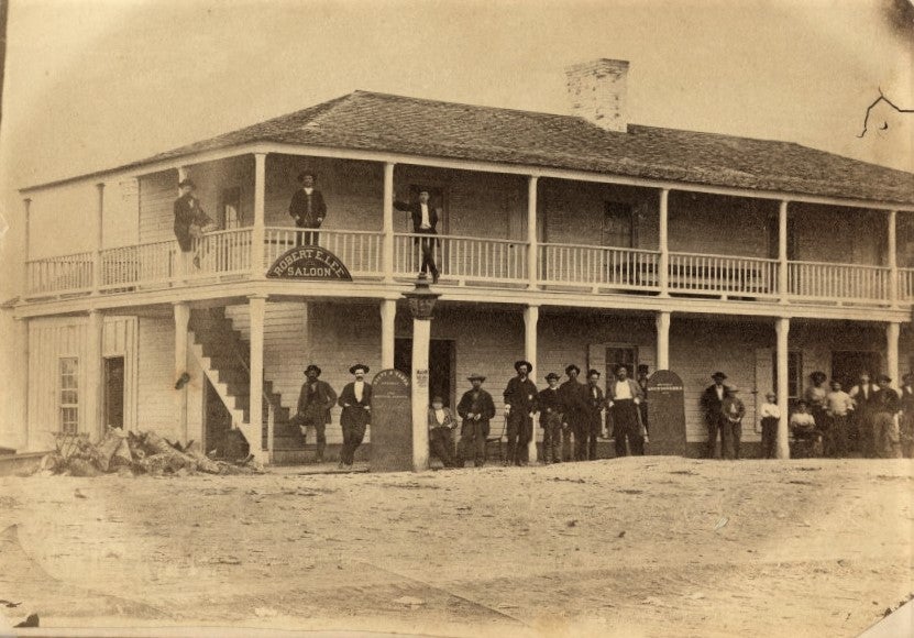 a black-and-white photo of a two-story wooden building with a wraparound porch
